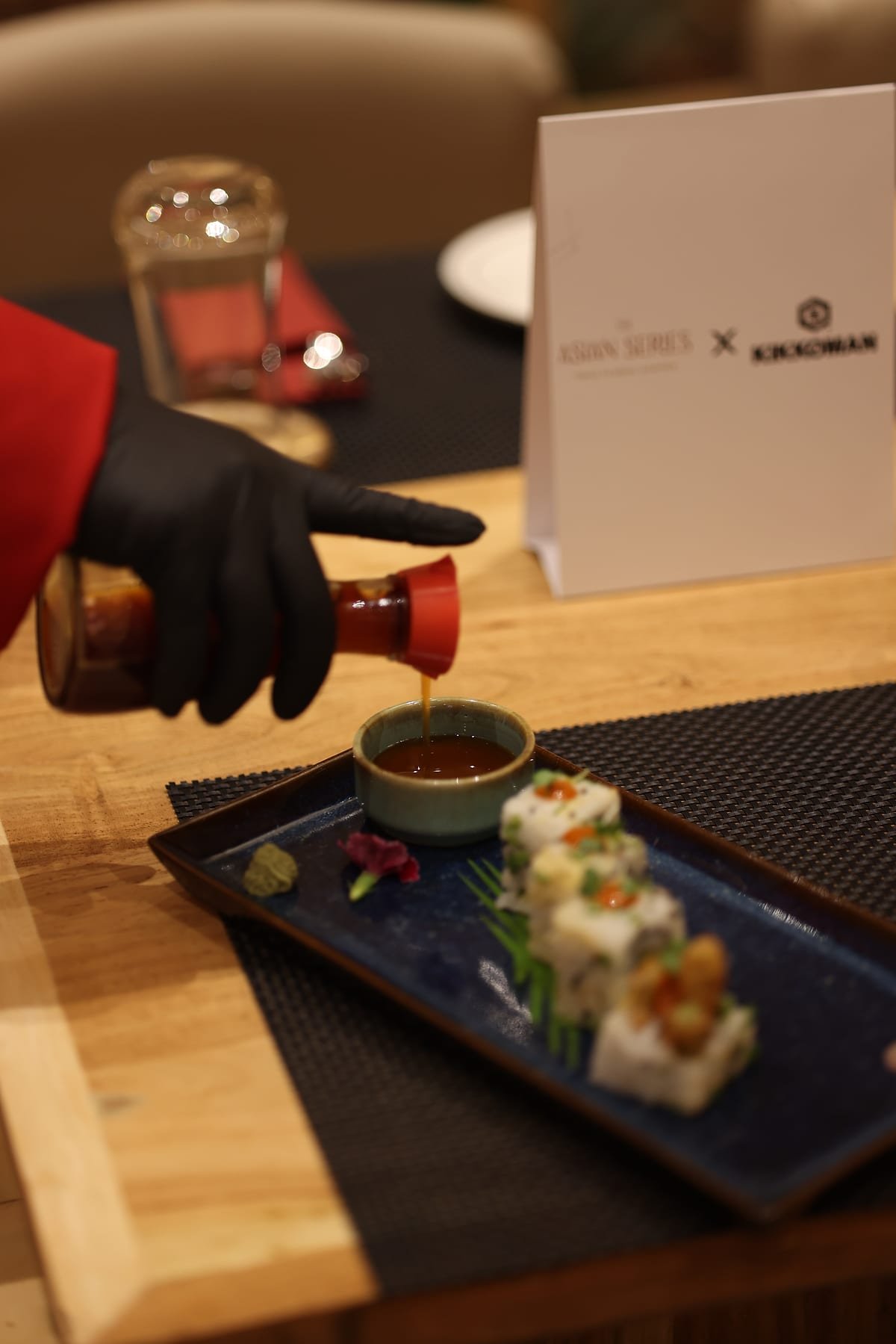 A chef finishing a plate of maki with a pour of sauce
