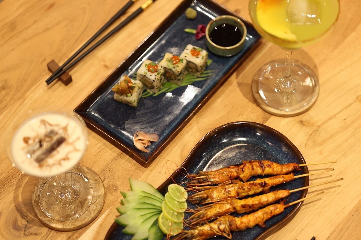 An overhead view of a full table — maki, prawn satay and cocktails