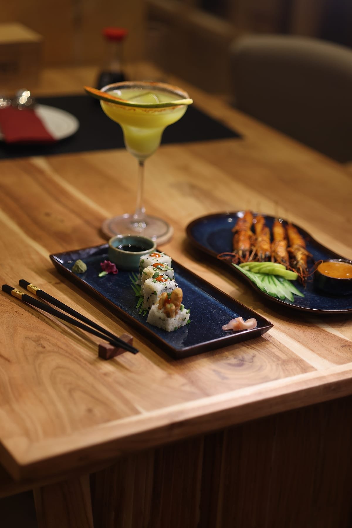 A cocktail on the table beside sushi and satay
